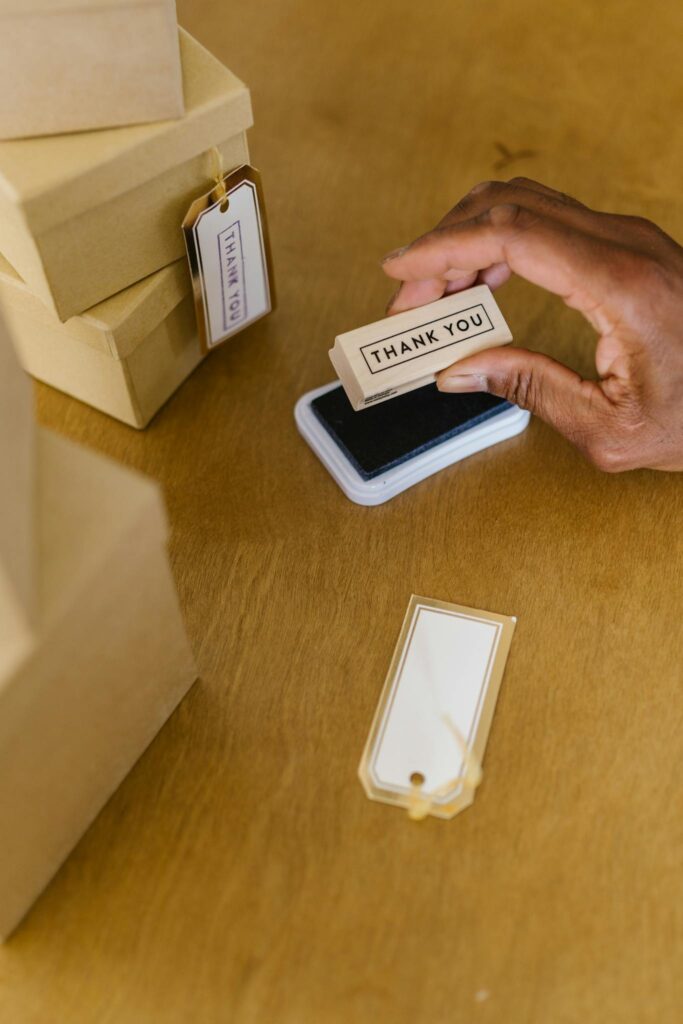 A person hand-stamps 'Thank You' tags for packaging cardboard boxes.